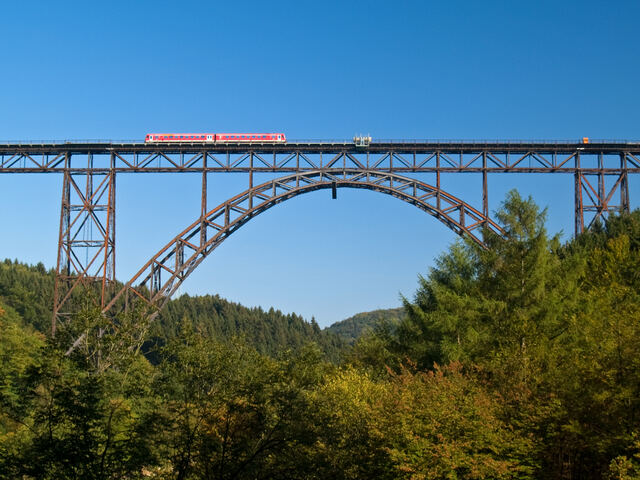 Müngstener Brücke mit rotem Zug über dem bewaldeten Tal