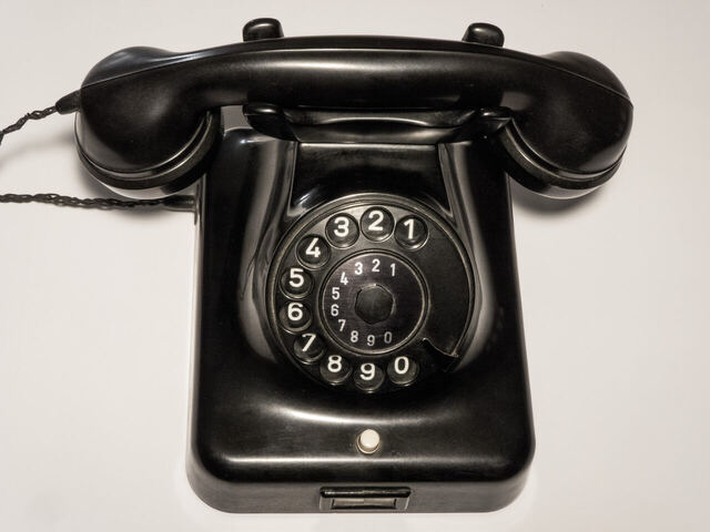 Schwarzes Tischtelefon mit Wählscheibe und aufgelegtem Hörer vor hellem Hintergrund.